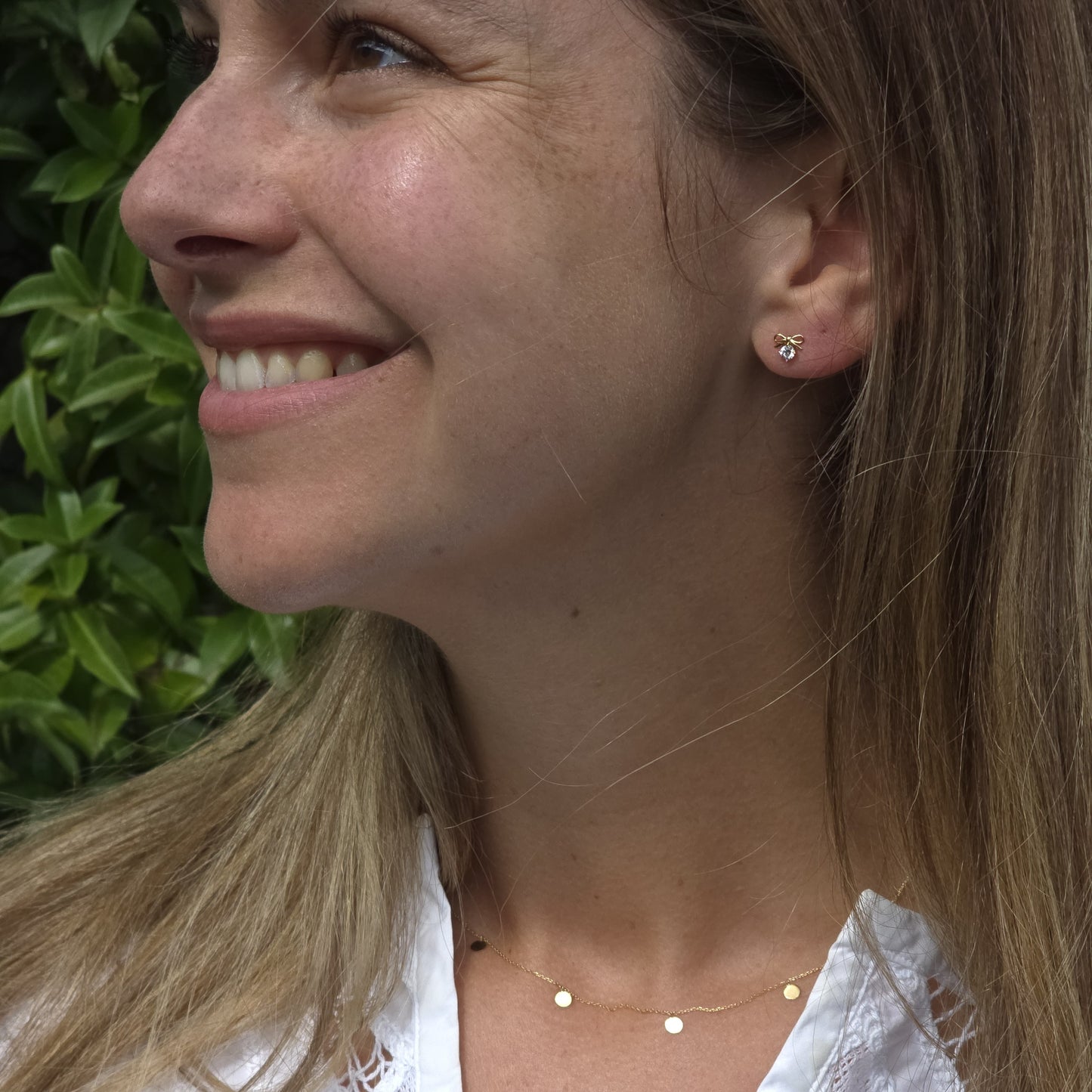 Woman wearing earrings and a necklace with a green leafy background
