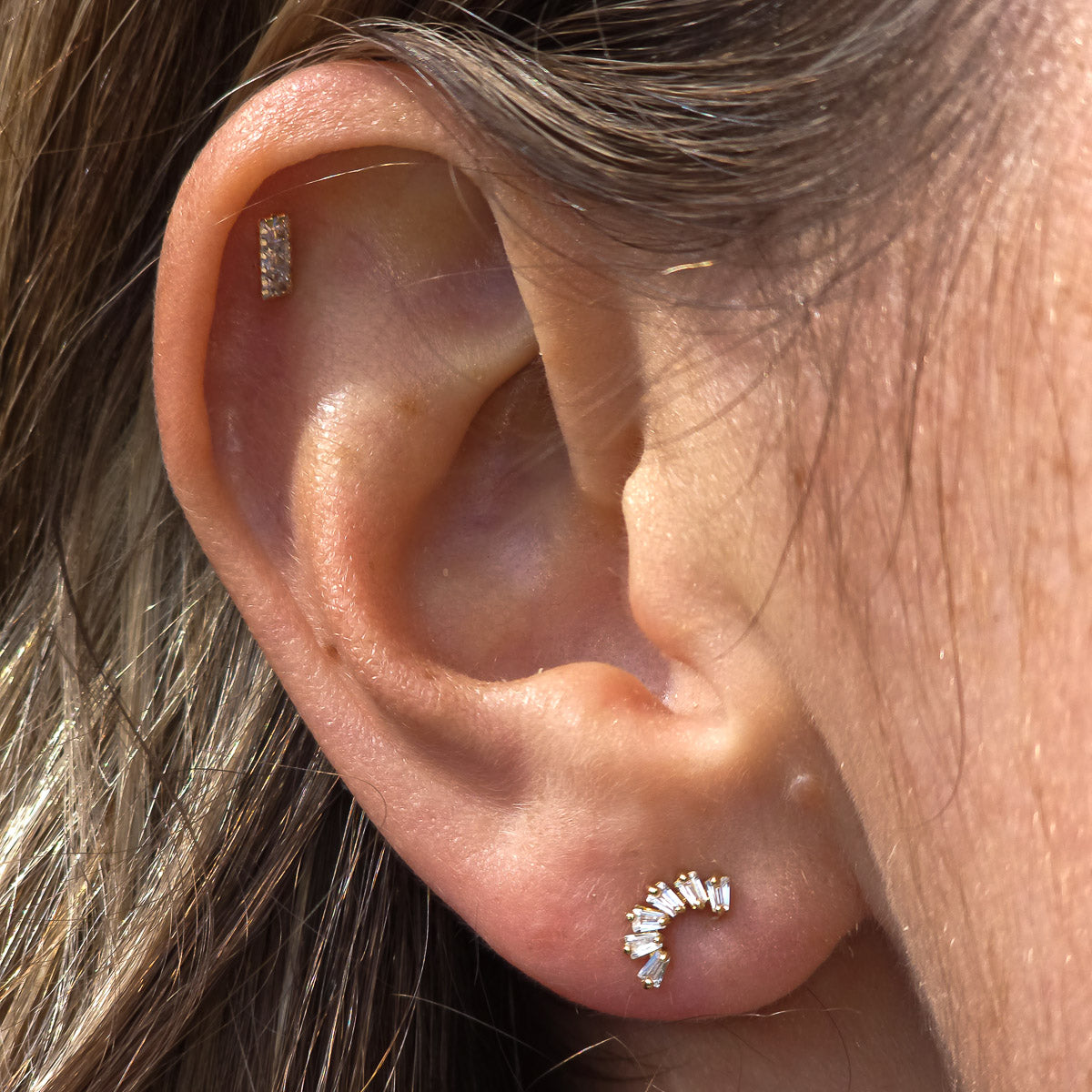 Close-up of an ear with two diamond stud earrings.