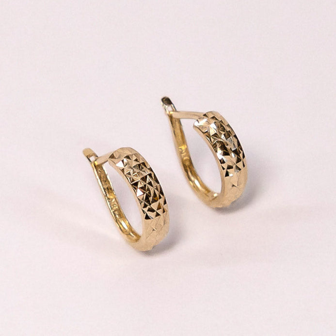 Gold hoop earrings on a light pink background