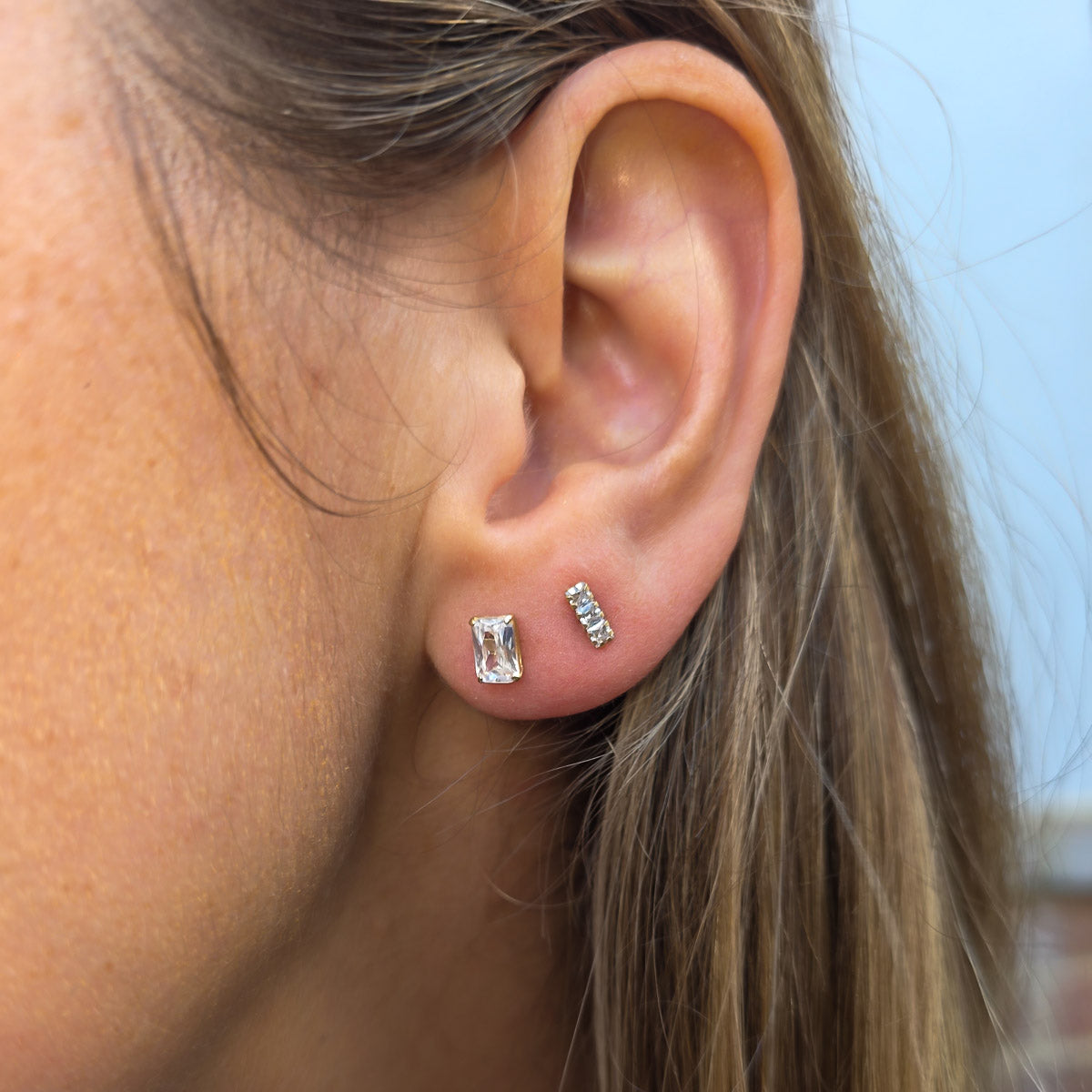 Close-up of an ear wearing two silver stud earrings with a blurred background