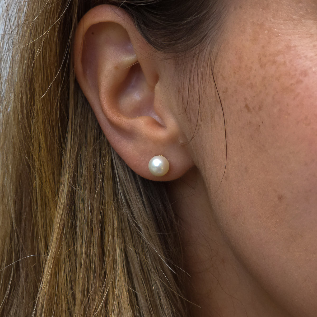 Close-up of an ear wearing a pearl earring with hair partially covering the frame.