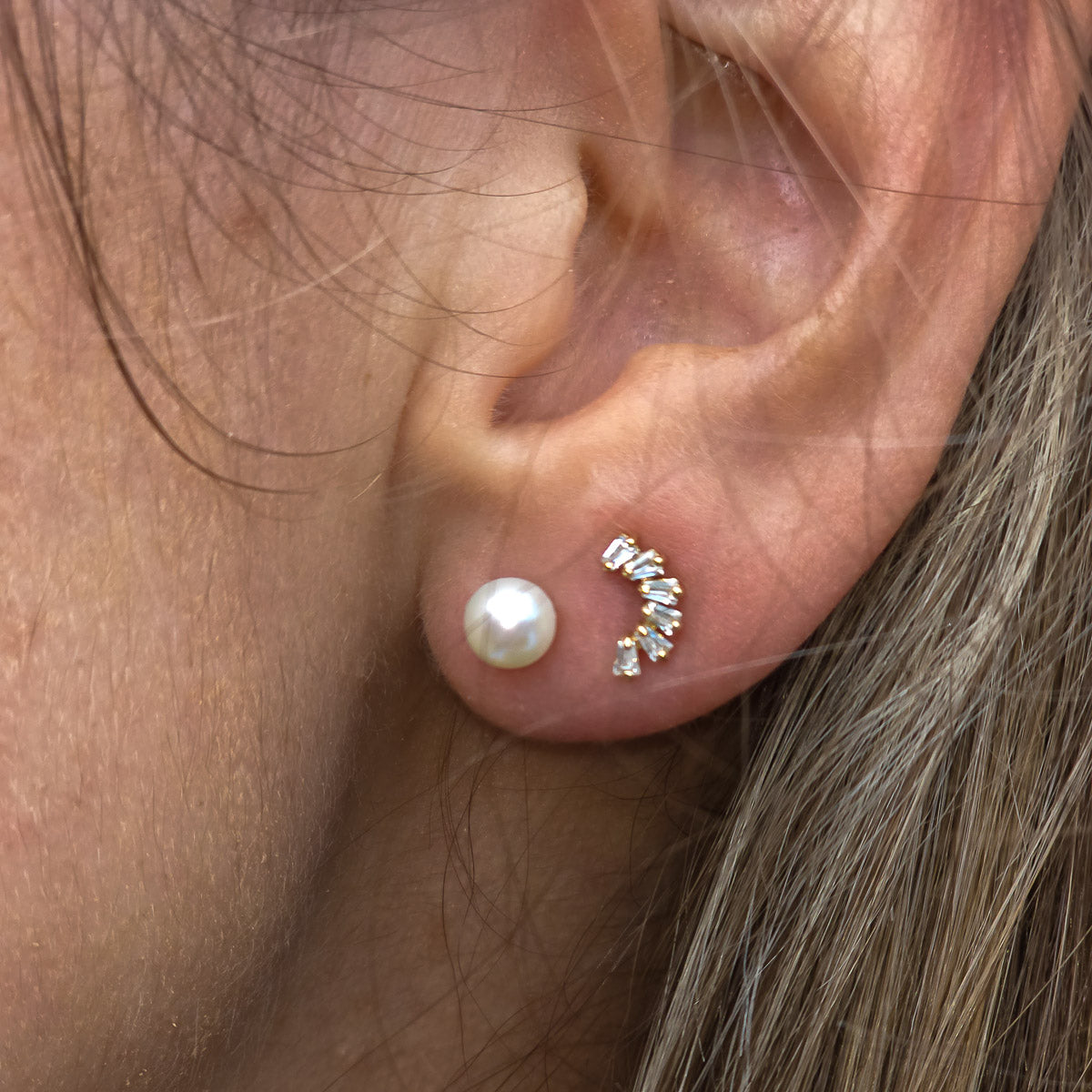 Close-up of an ear wearing a pearl earring and a diamond-studded earring.