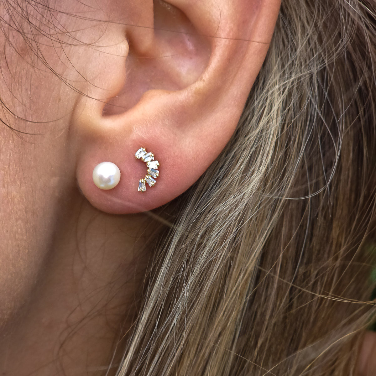 Close-up of an ear wearing a pearl earring and a diamond-studded earring.