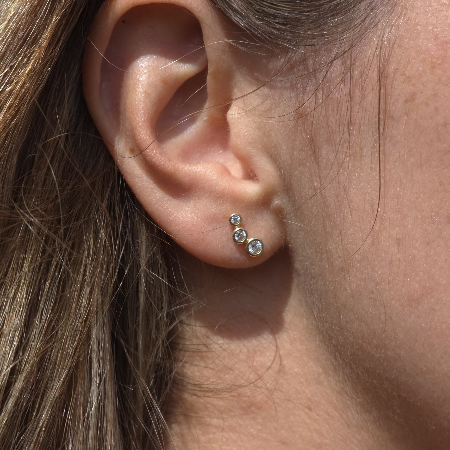 Close-up of an ear wearing a set of gold earrings with small gemstones.
