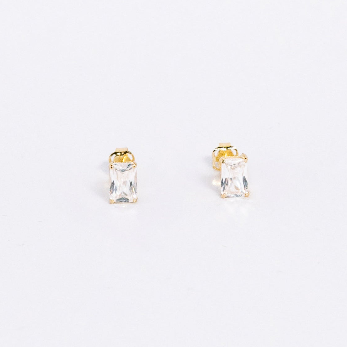 Small gold and clear gemstone stud earrings on a white background