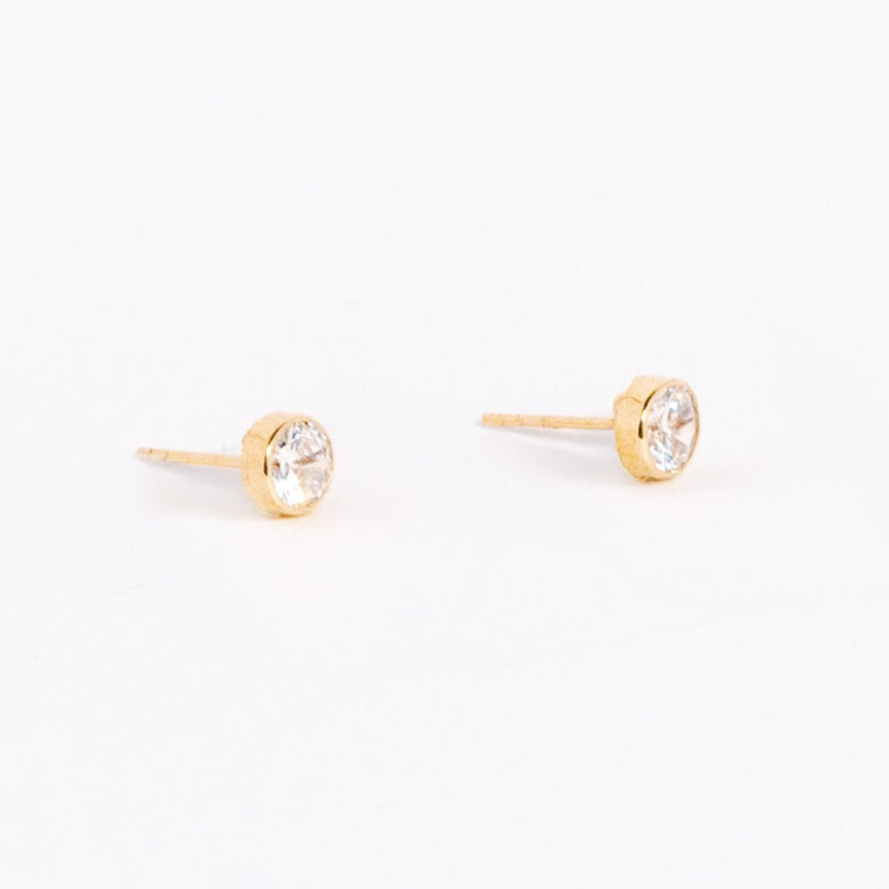 Gold stud earrings with clear gemstones on a light pink background