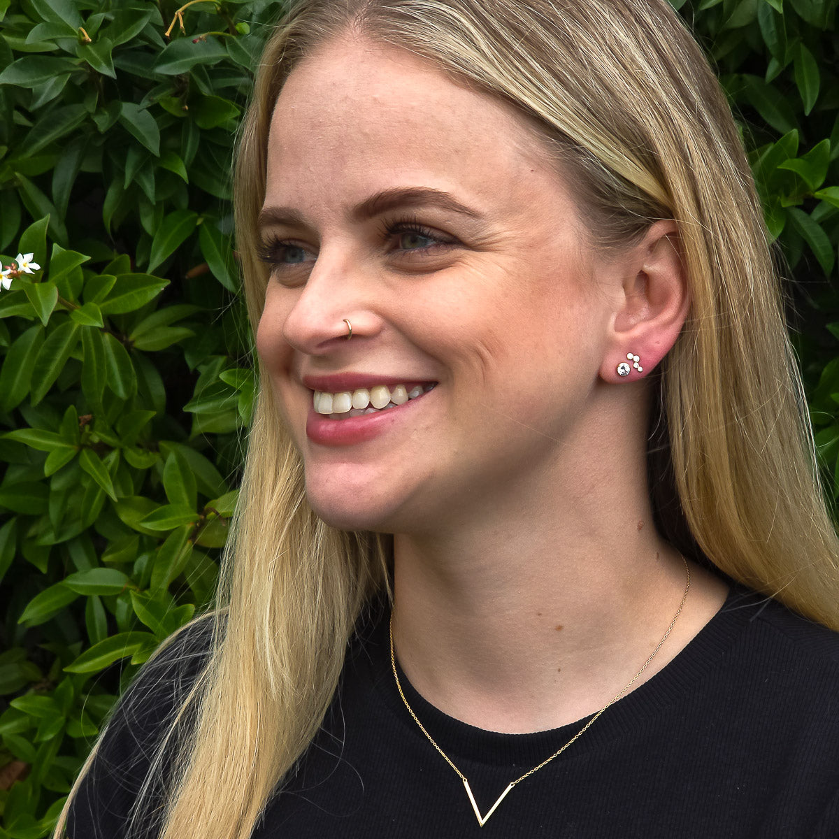 Woman with blonde hair and a black shirt standing in front of green foliage