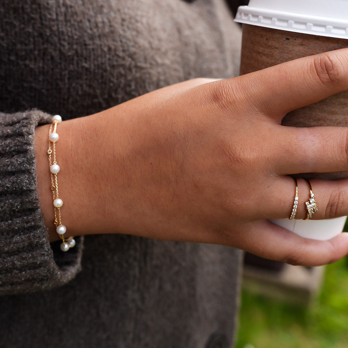 Hand wearing a pearl bracelet and ring, holding a coffee cup.