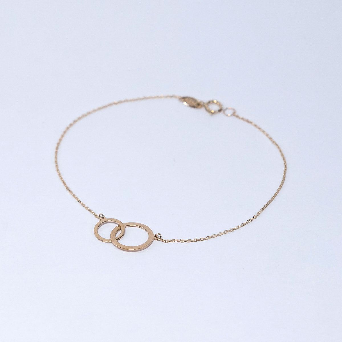 Gold bracelet with interlocking rings on a light blue background