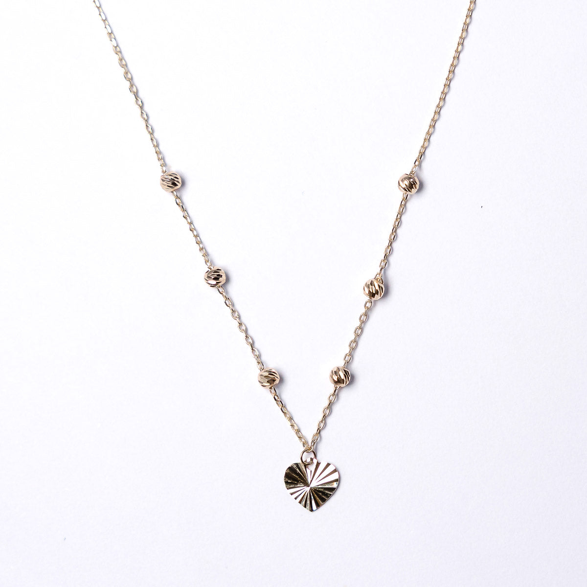 Gold necklace with a heart-shaped pendant on a white background