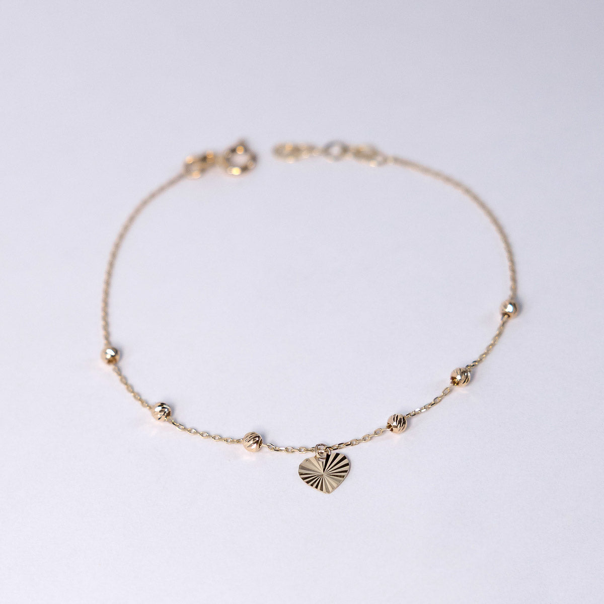 Gold bracelet with a heart-shaped charm on a light gray background
