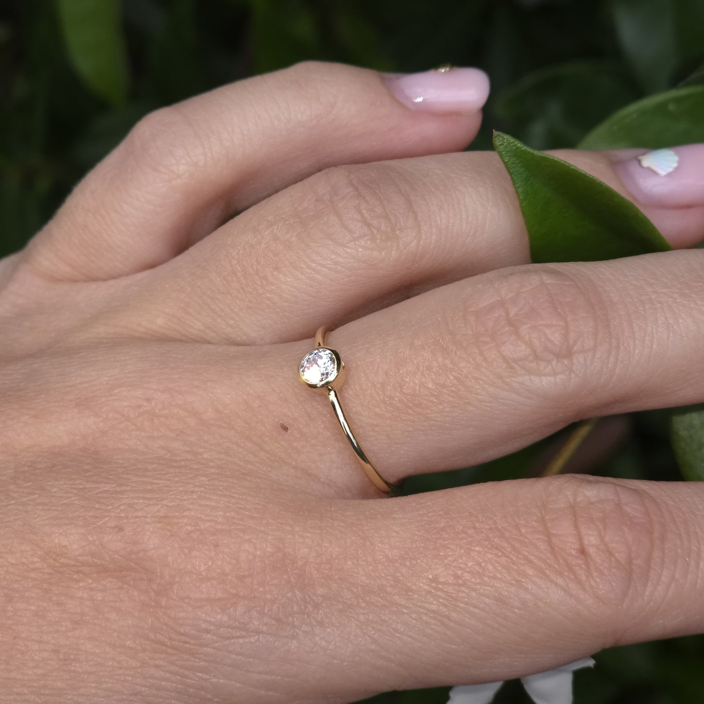 Gold ring with a diamond on a person's finger against a green leafy background