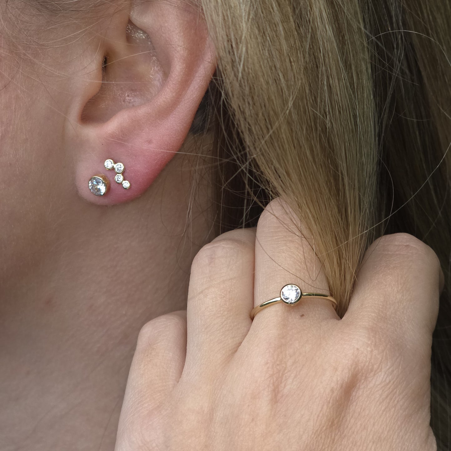 Close-up of a person wearing gold earrings and a ring with a diamond.