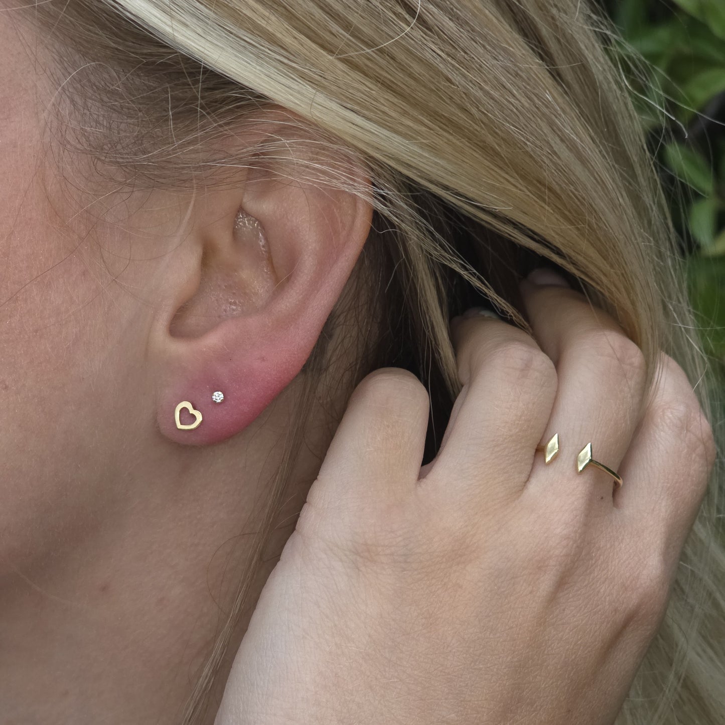 Close-up of an ear with gold earrings and a hand wearing a gold ring.