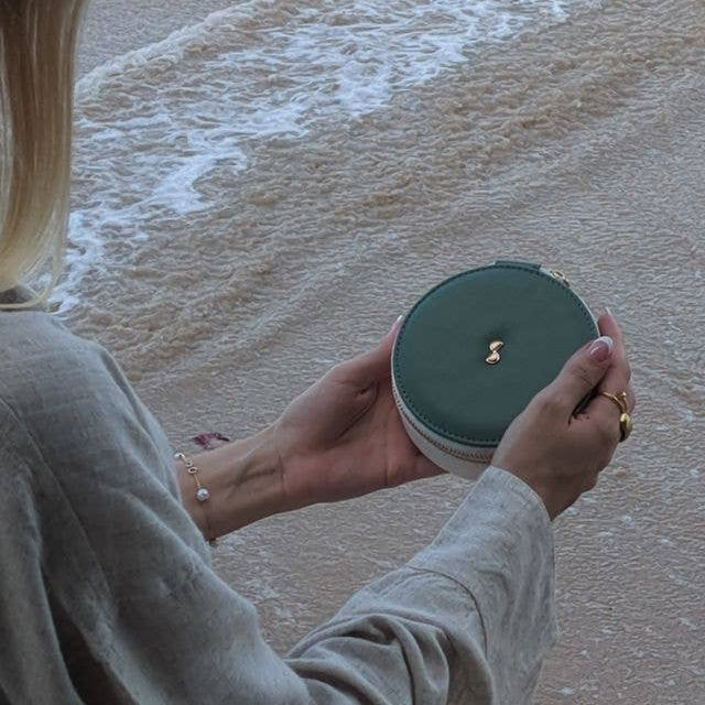 Person holding a medium green Stackers round travel jewellery box on a beach with waves in the background