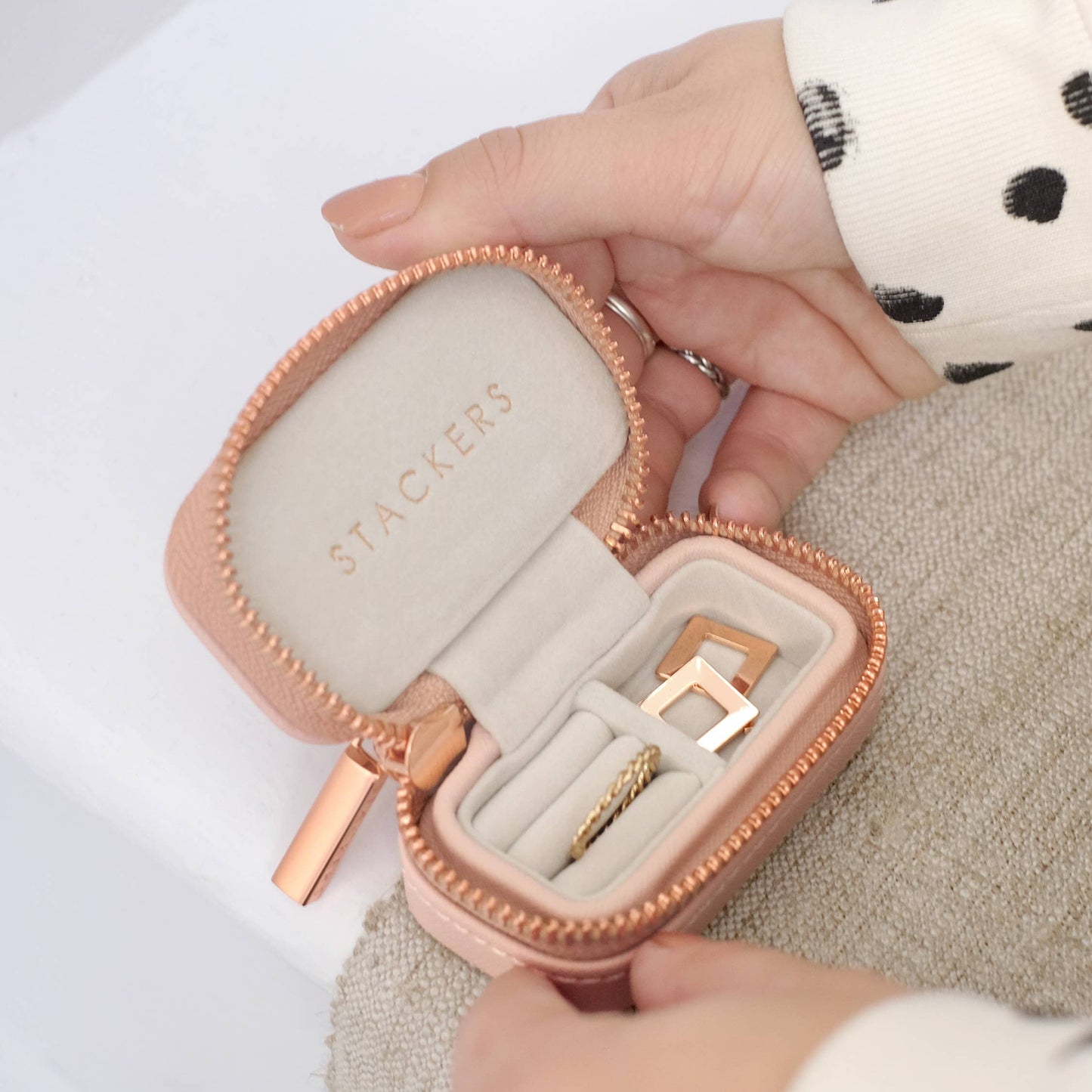 Hand holding a mini blush travel jewellery box with 'Stackers' branding, containing gold rings.