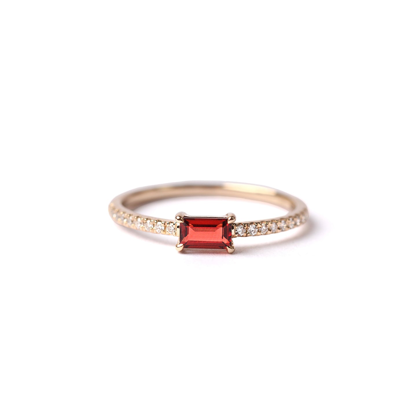 Women's solid yellow gold ring set with a central baguette cut red garnet, with small round diamonds each side set into the shoulders of the band, displayed laying down, facing frontwards on a white background.