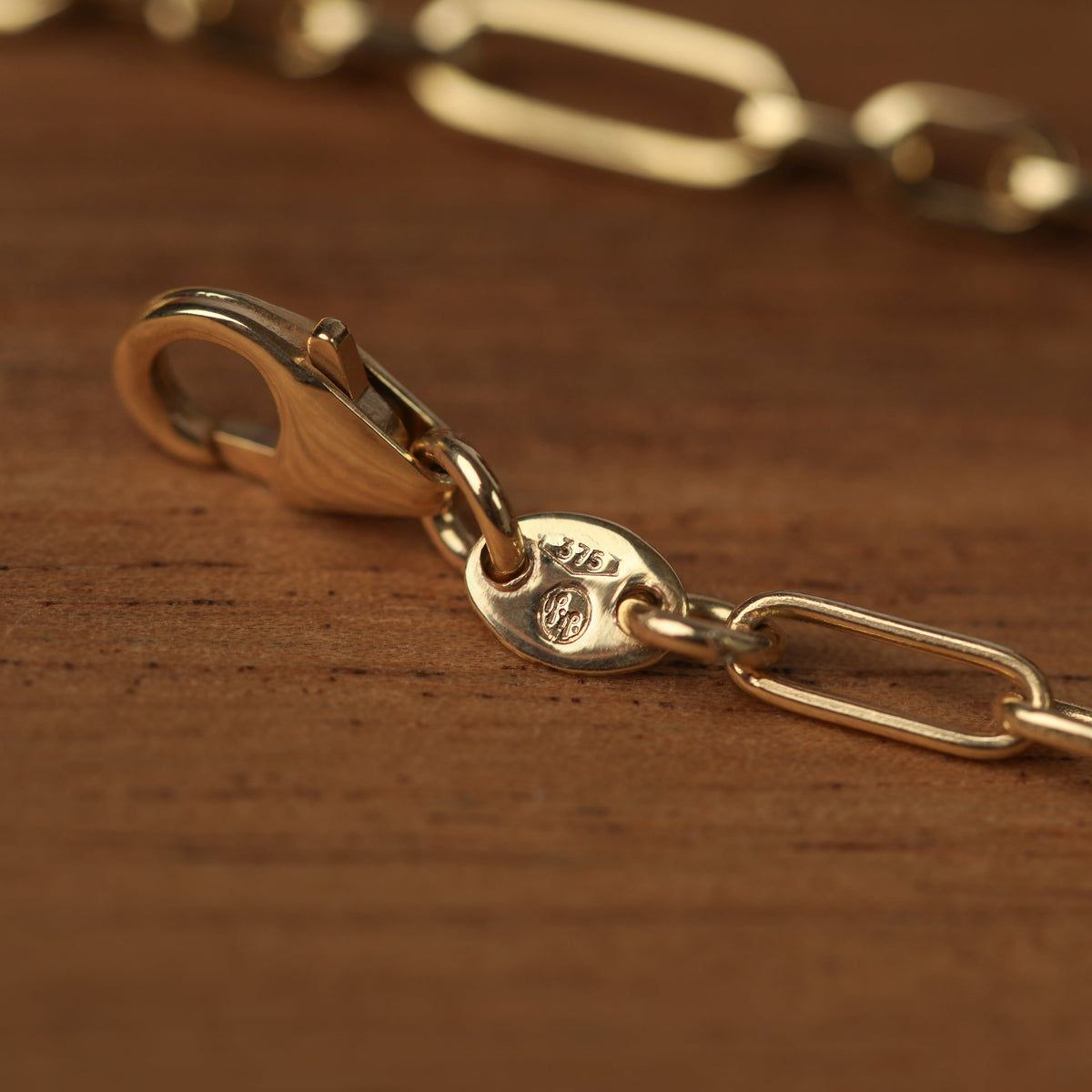 Women's solid yellow gold paperclip chain bracelet featuring the clasp displayed on a wooden background.