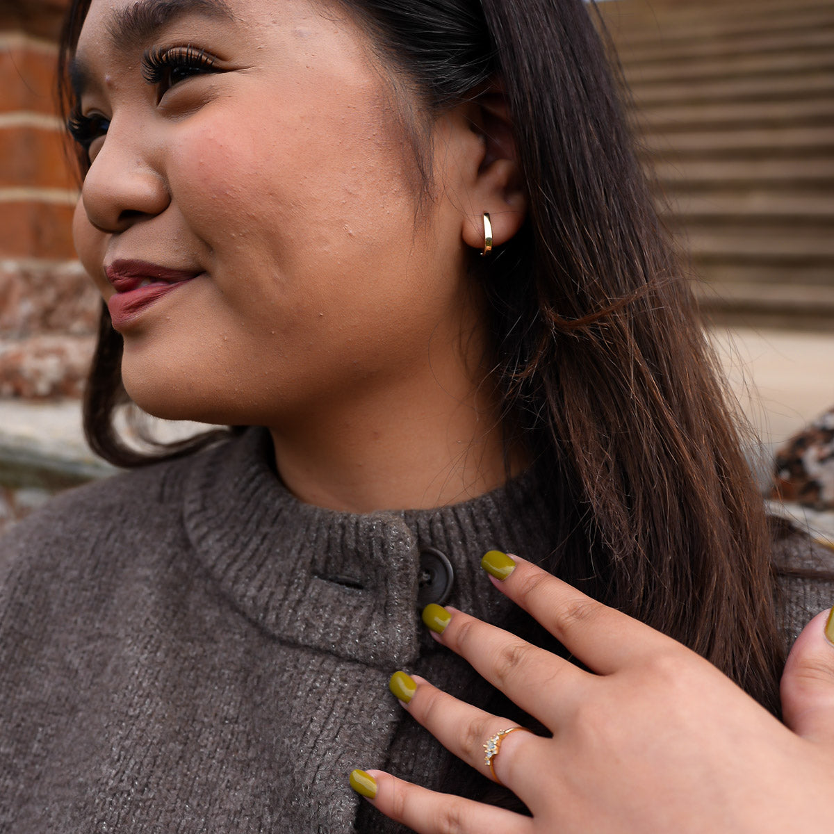 Woman wearing a gray sweater with a hand touching her shoulder, outdoor setting