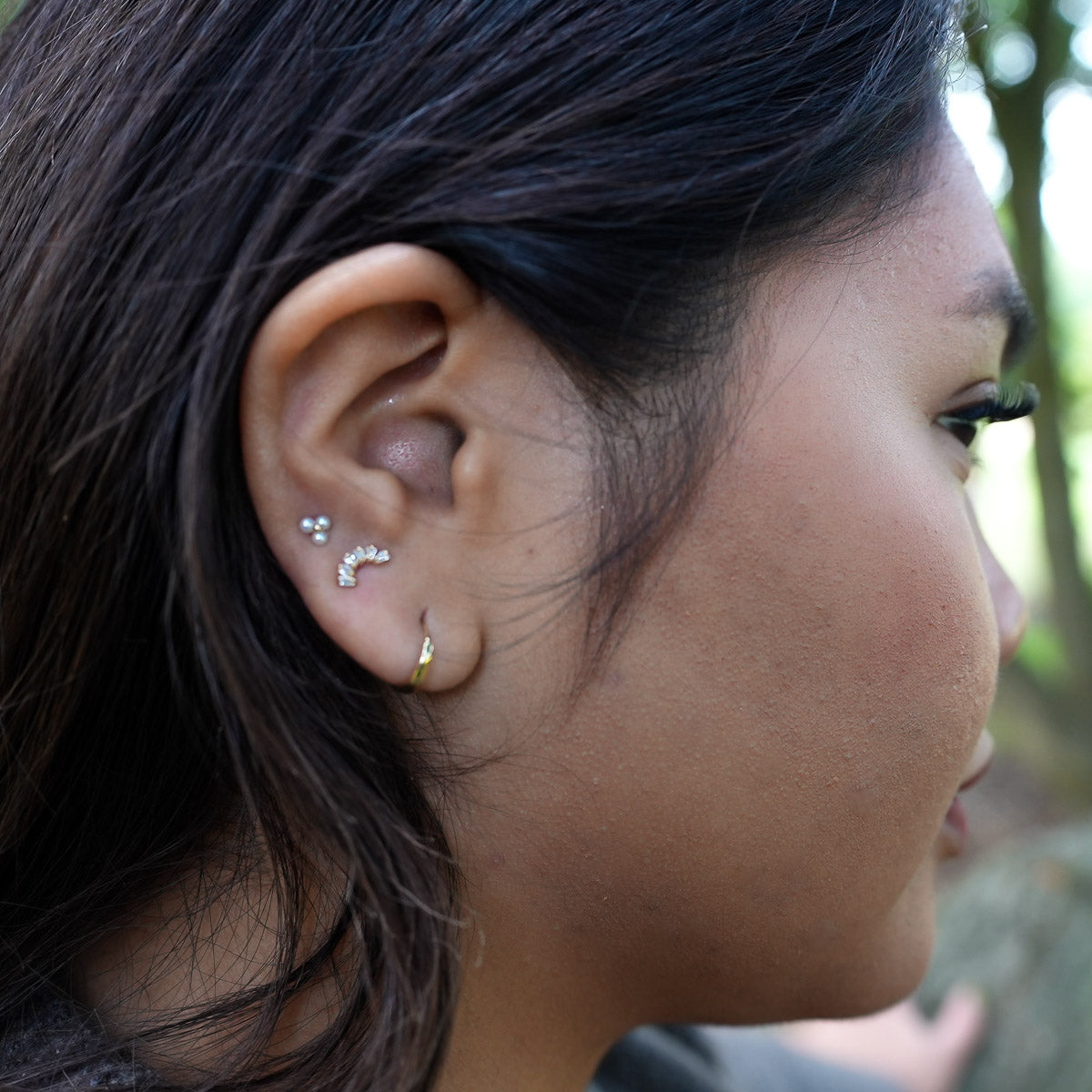 Close-up of a person's ear with earrings, outdoors.