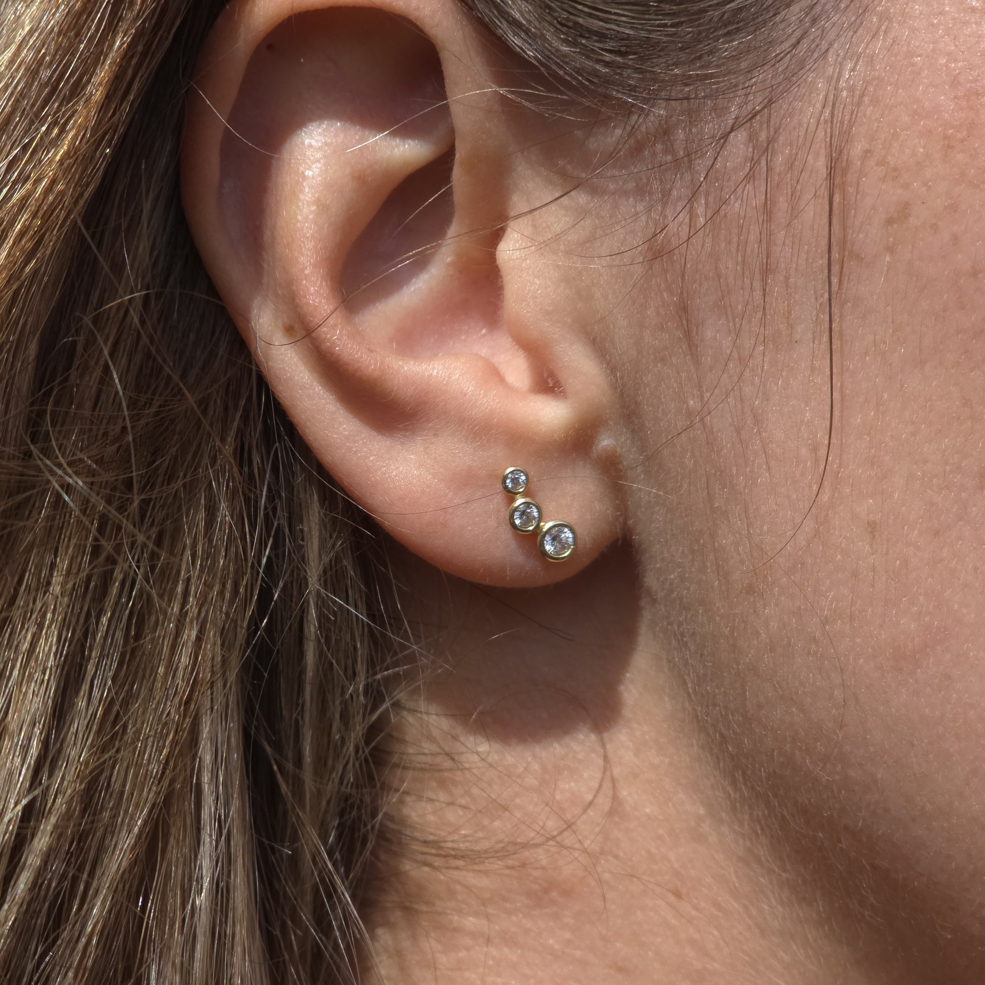 Close-up of an ear wearing a set of gold earrings with small gemstones.