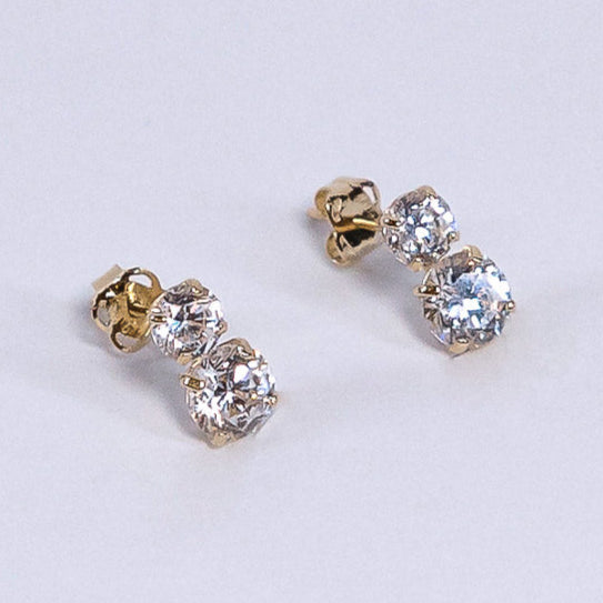 Pair of gold and crystal stud earrings on a light gray background