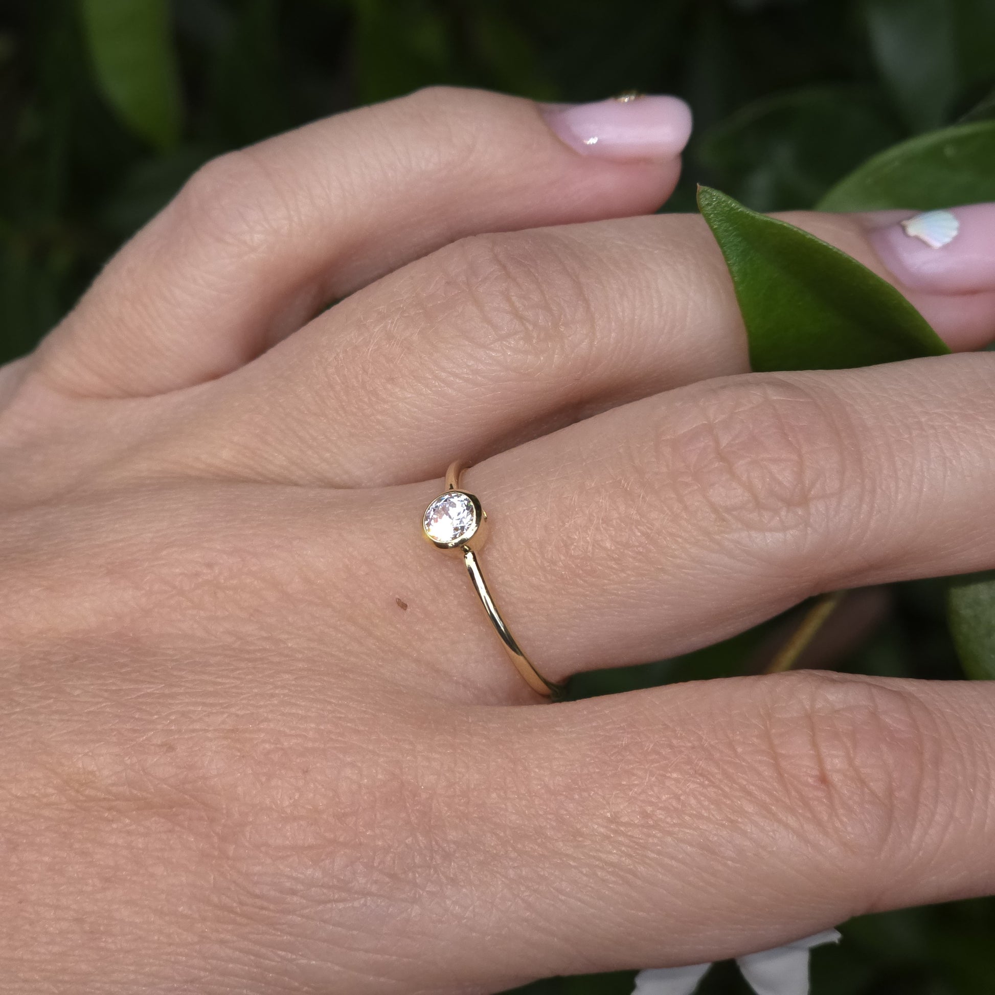 Gold ring with a diamond on a person's finger against a green leafy background