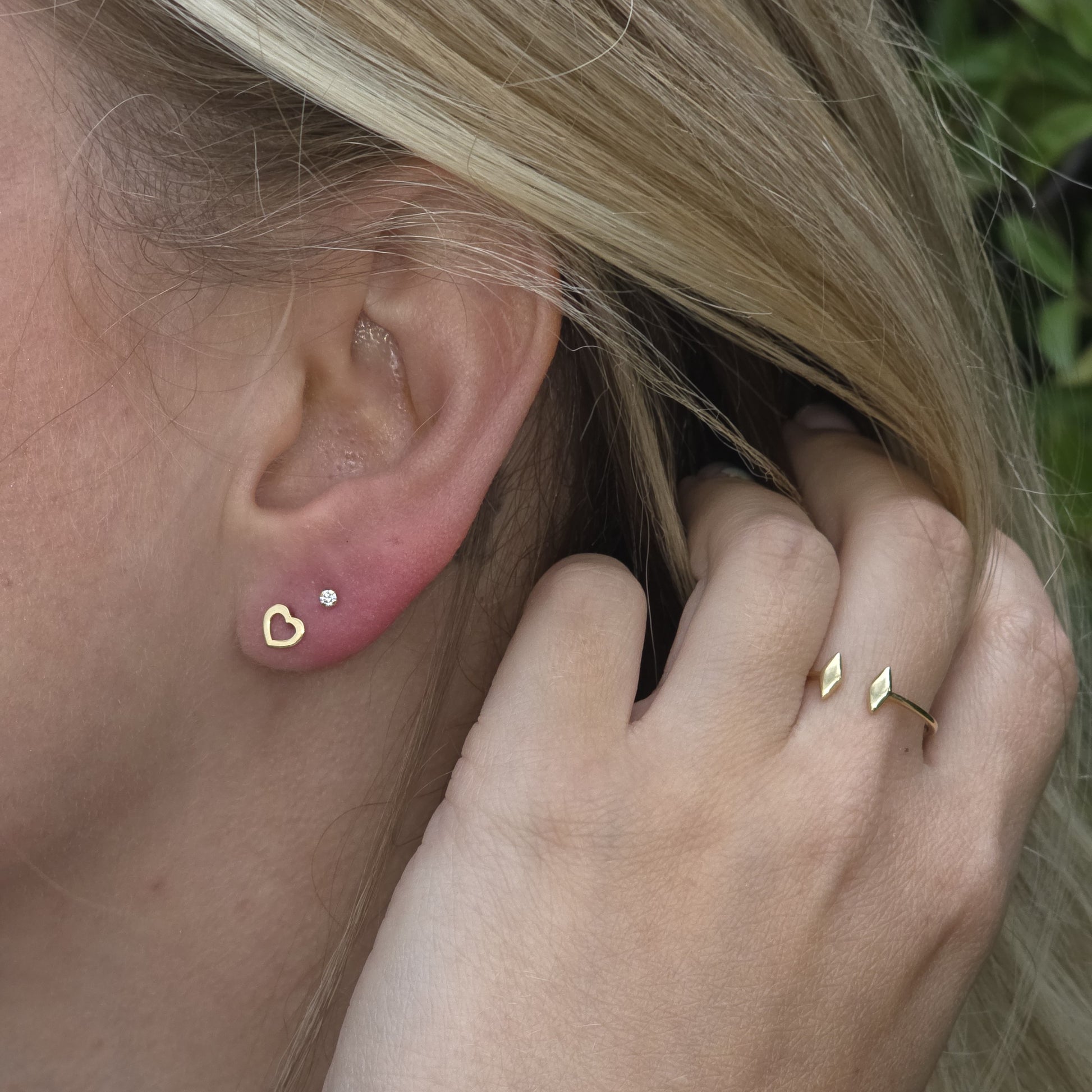 Close-up of an ear with gold earrings and a hand wearing a gold ring.