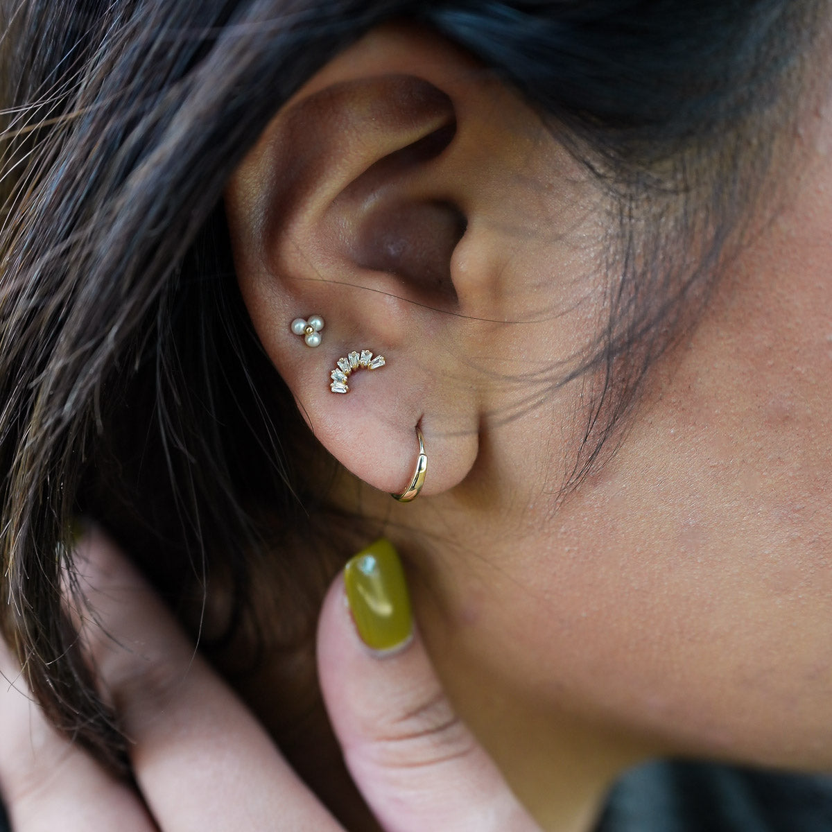Close-up of an ear with multiple earrings and a hand touching the earlobe.
