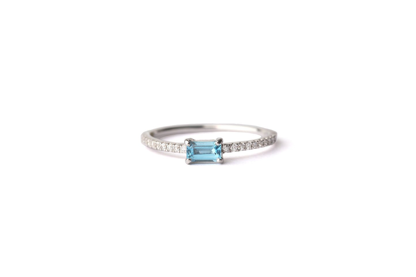 Women's blue topaz gemstone in a baguette setting on a slim white gold band set with diamonds on the shoulders, displayed on a white background.