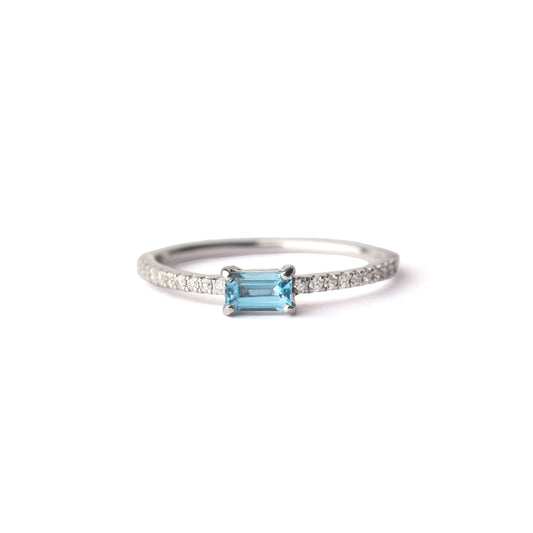 Women's blue topaz gemstone in a baguette setting on a slim white gold band set with diamonds on the shoulders, displayed on a white background.