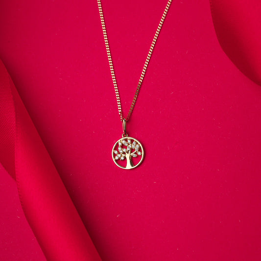Gold necklace with a tree pendant on a red fabric background