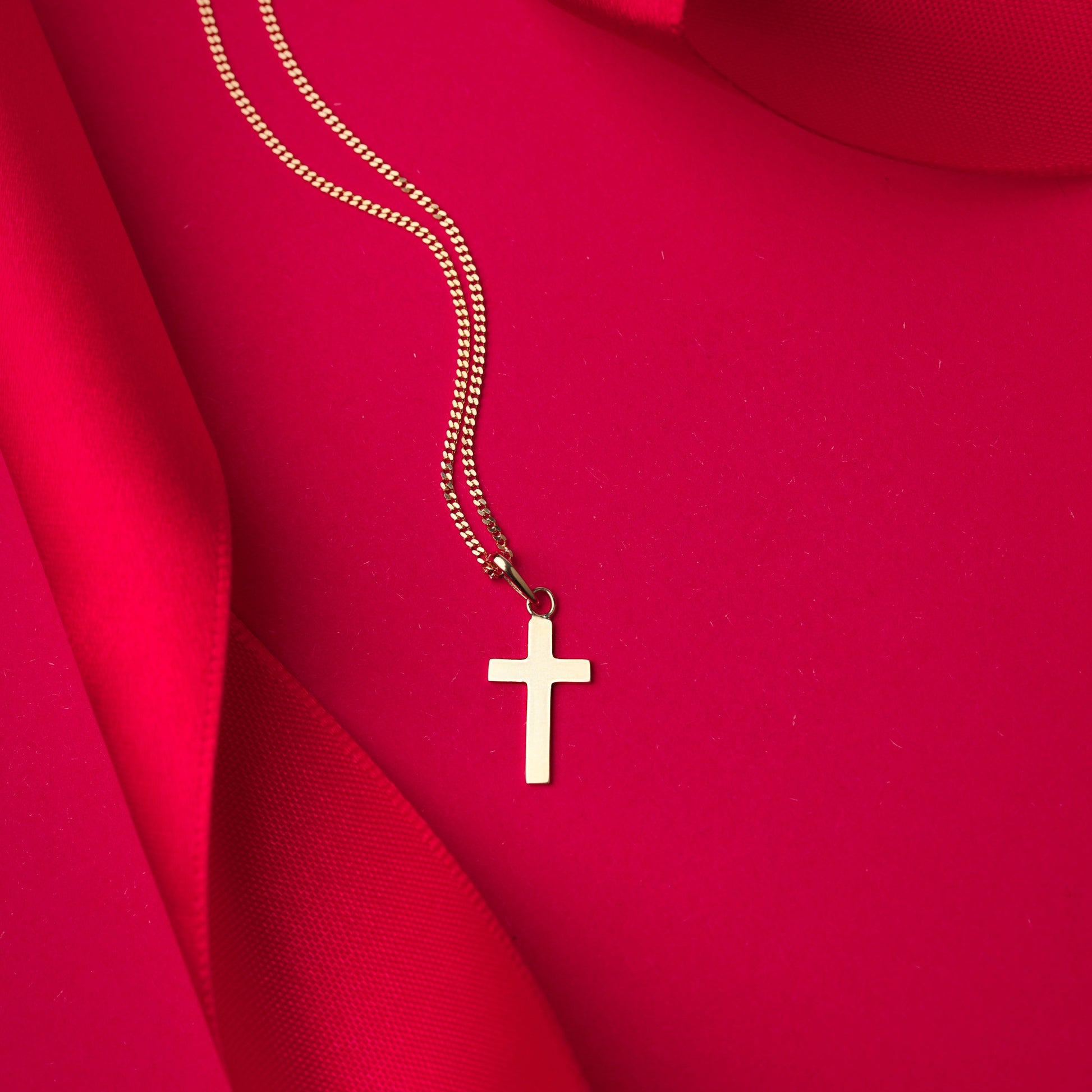 Gold necklace with a cross pendant on a red fabric background
