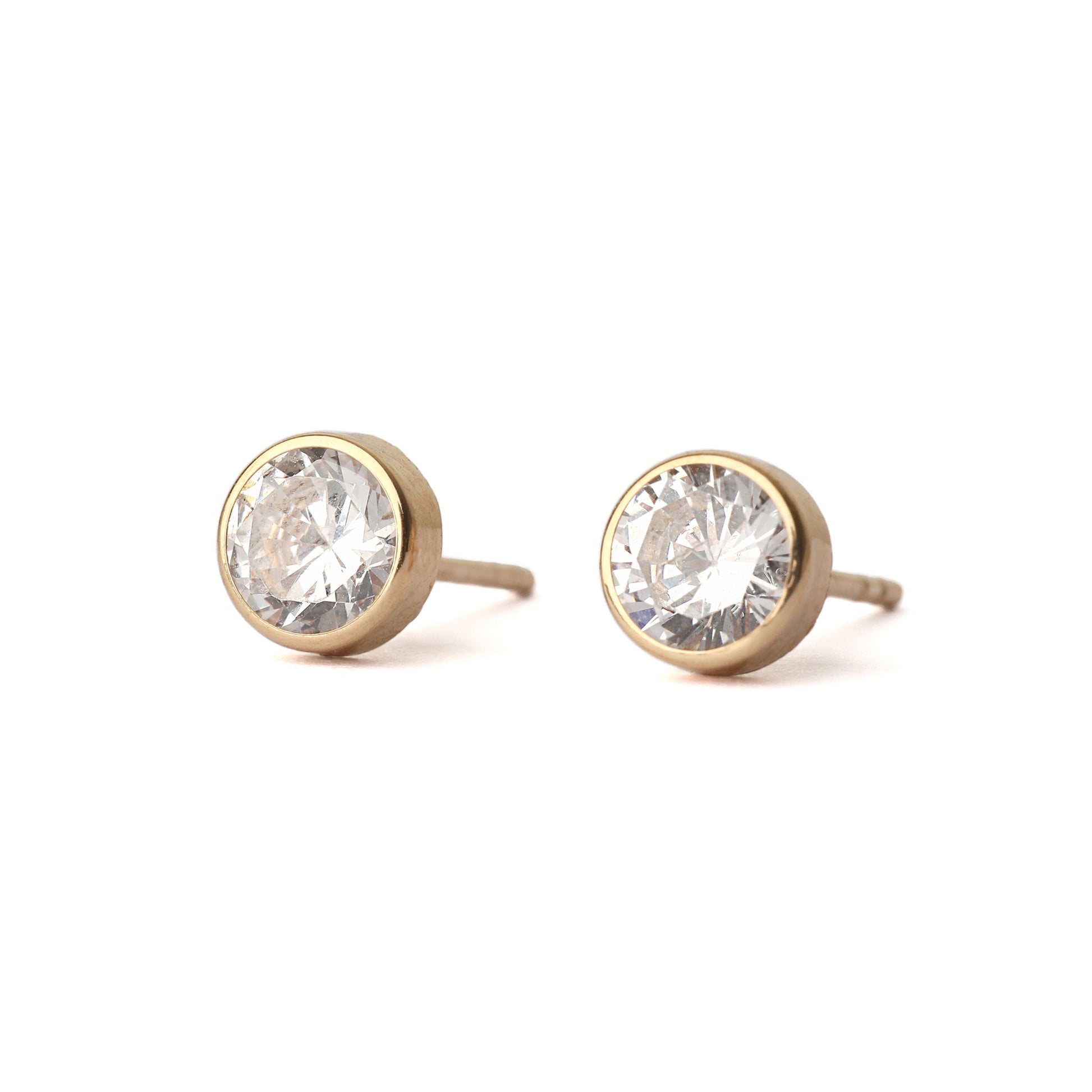 Women's pair of solid yellow gold stud earrings, each with a cubic zirconia gemstones in a bezel setting.  The earrings are displayed facing forward on a white background