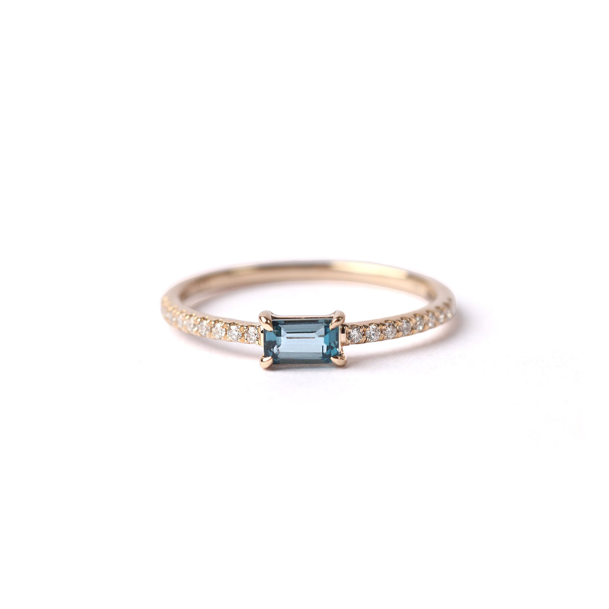 Women's solid yellow gold ring set with a central London blue topaz gemstone and small round diamonds on the shoulders each side of the topaz, displayed on a white background facing frontwards laying on it's side.