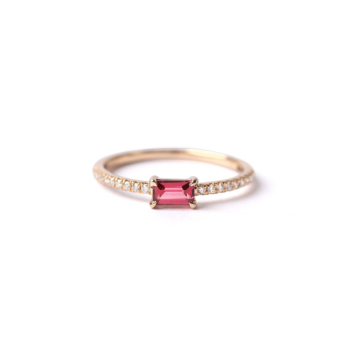 Women's solid yellow gold ring set with a central pink tourmaline gemstone and small round diamonds on the shoulders each side of the tourmaline, displayed on a white background laying on it's side facing frontwards.