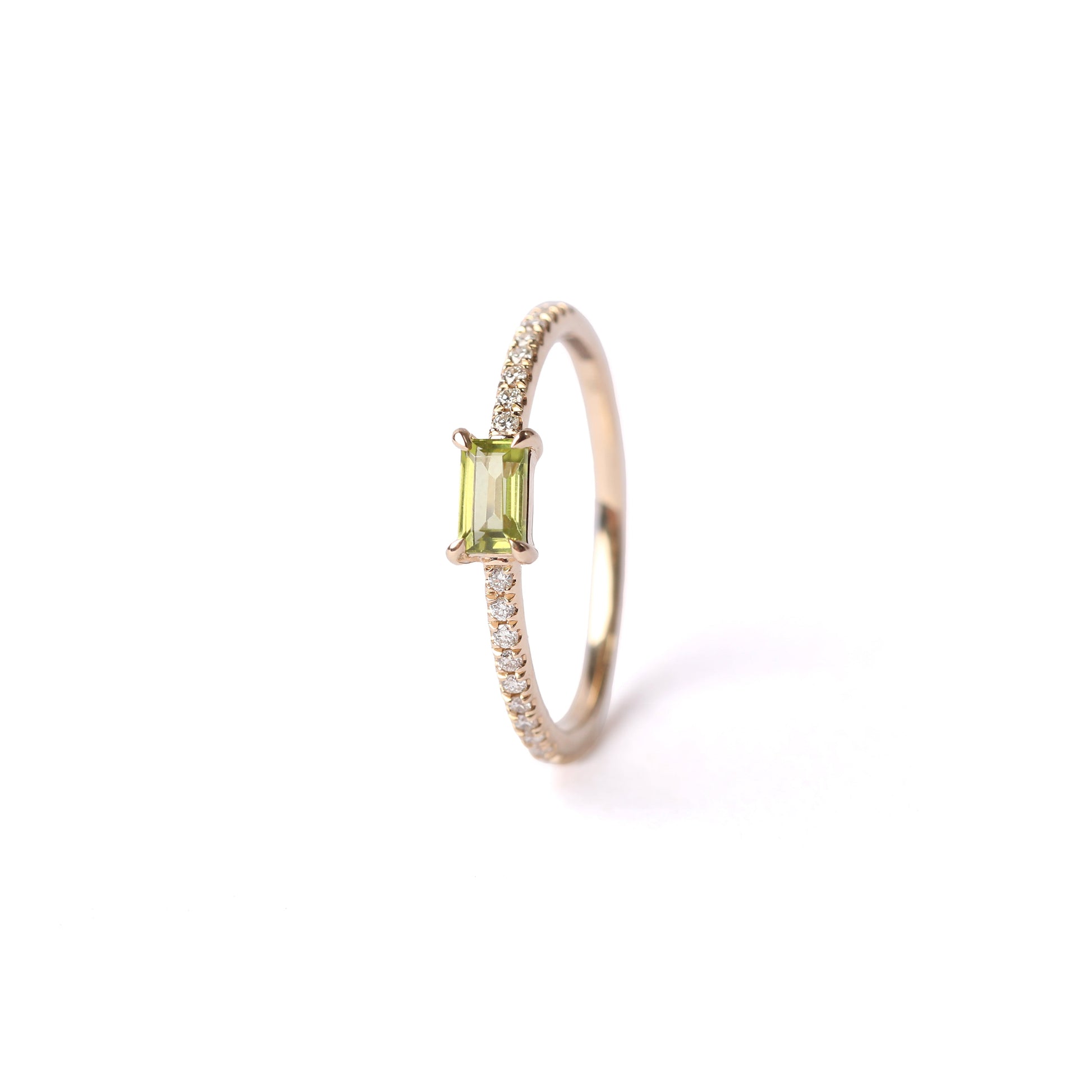 Women's solid yellow gold ring set with a central green peridot gemstone and small round diamonds on the shoulders each side of the peridot, displayed on a white background facing forwards standing up.