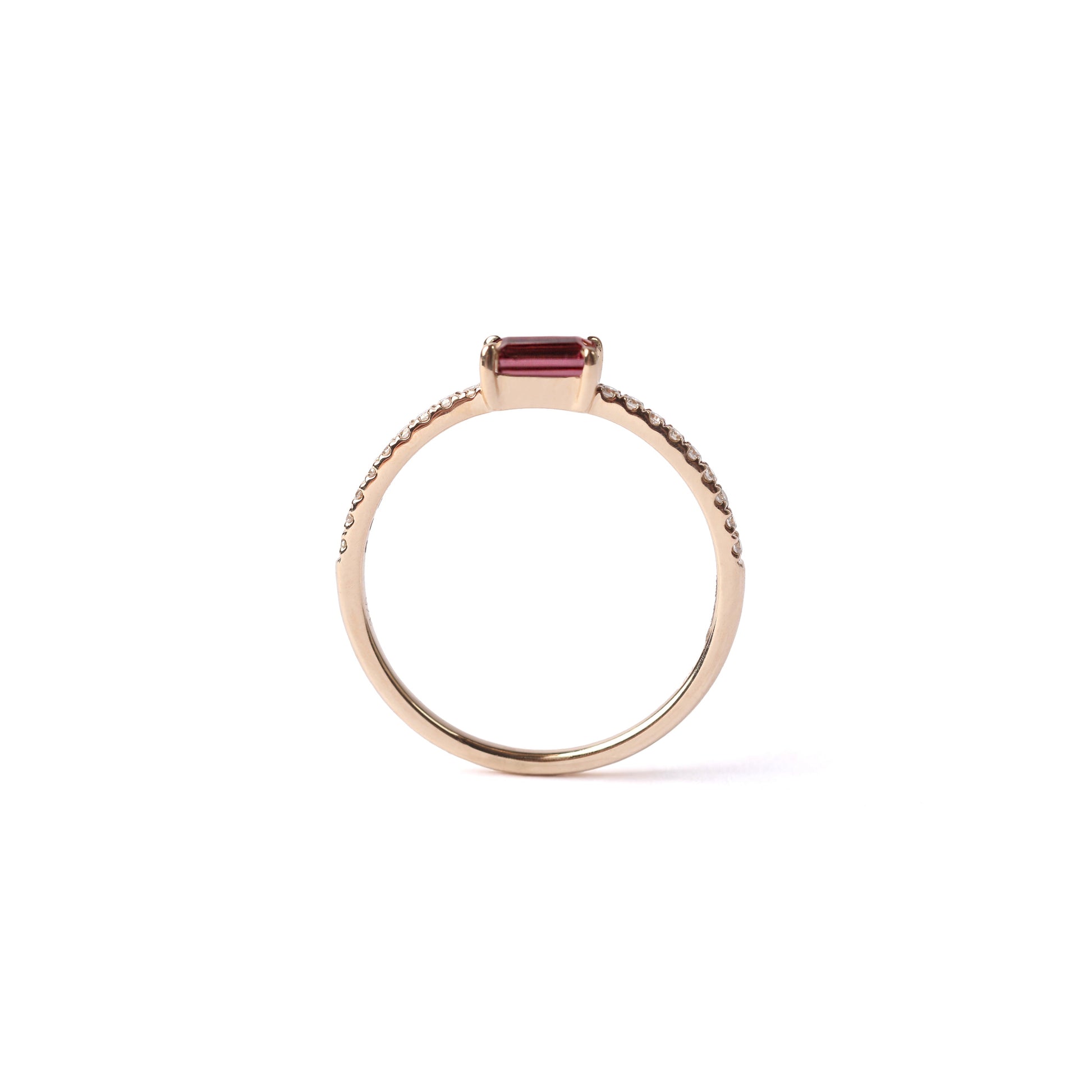 Women's solid yellow gold ring set with a central baguette cut pink tourmaline gemstone, with small round diamonds set into the shoulders on the ring on either side of the tourmaline, displayed standing up on the white background.