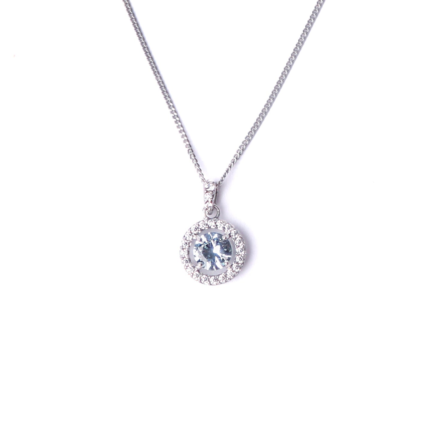 Women's sterling silver and cubic zirconia gemstone pendant, set with a large clue gemstone surrounded by smaller clear cubic zirconia gemstones hanging on a silver chain all set on a white background.