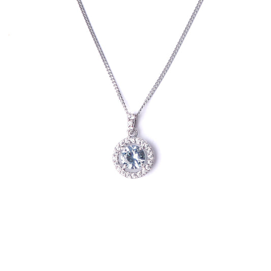 Women's sterling silver and cubic zirconia gemstone pendant, set with a large clue gemstone surrounded by smaller clear cubic zirconia gemstones hanging on a silver chain all set on a white background.