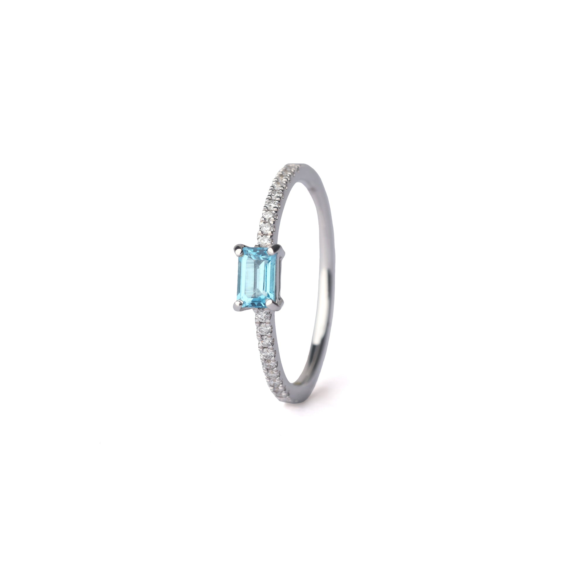 Women's white gold stacking ring set with a baguette cut blue topaz gemstone centrally and diamonds on the shoulders, displayed on a white background.