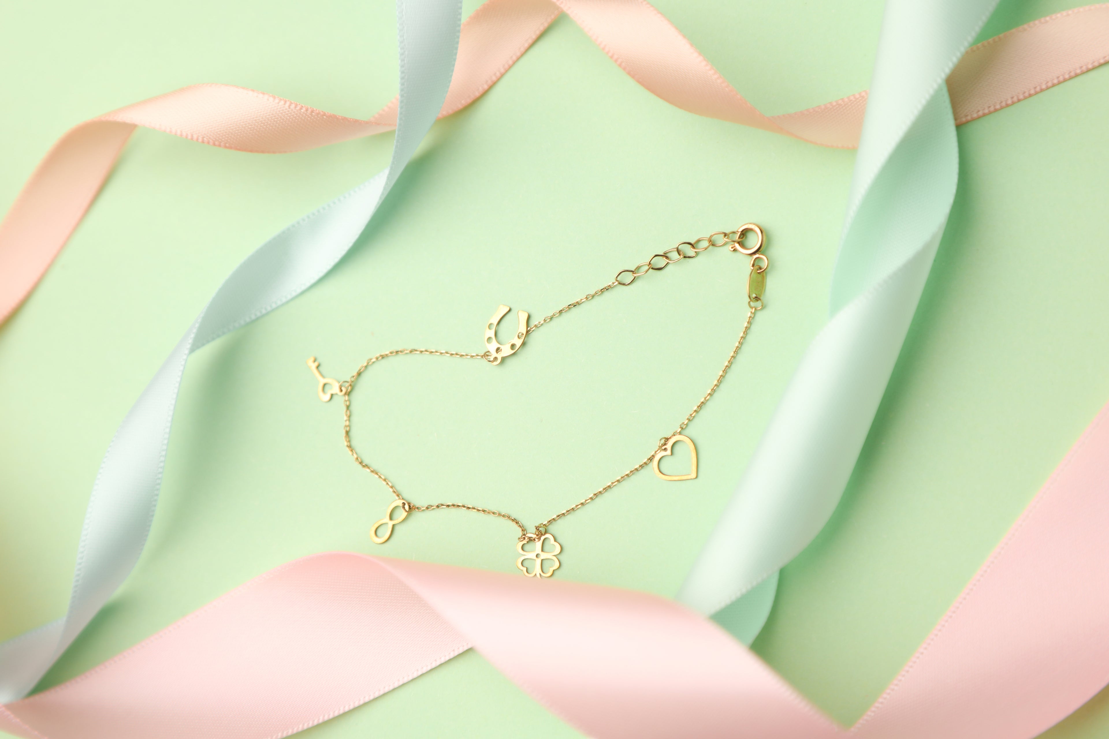 Solid gold bracelet with lucky charms on a green background with pastel coloured ribbons