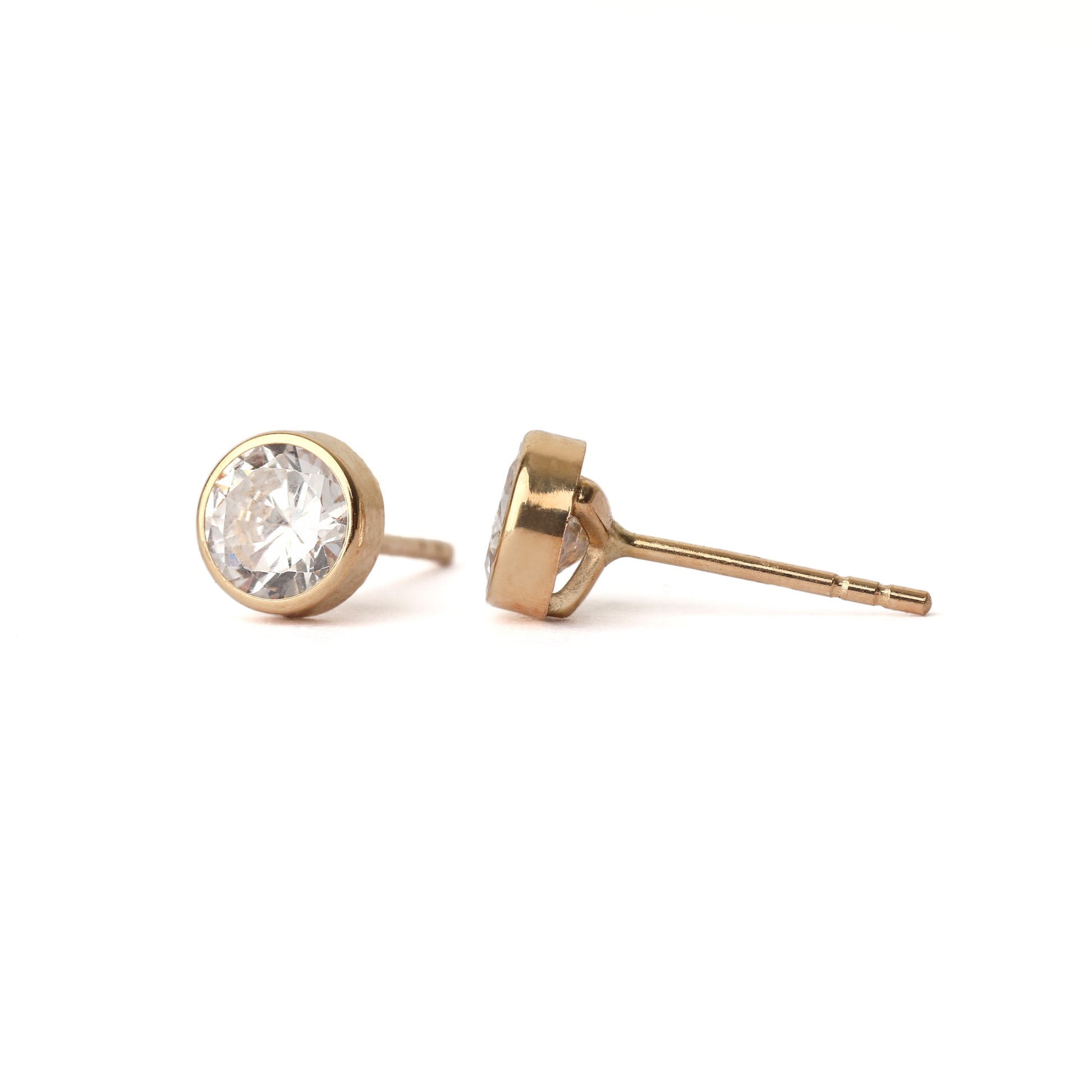 A pair of women's solid gold stud earrings each set with a single cubic zirconia, displayed straight on and sideways on on a white background