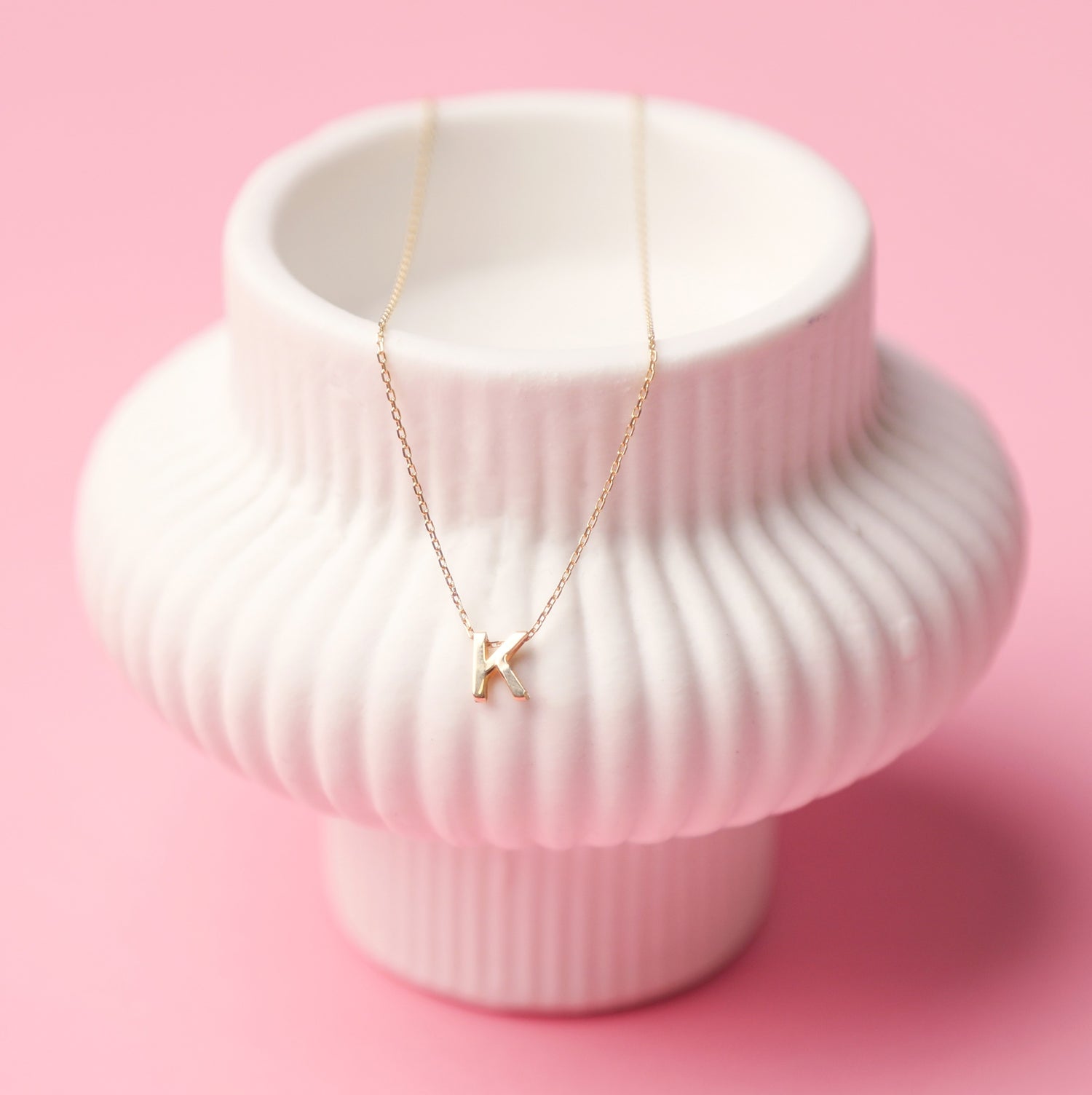 White ribbed vase with a gold necklace draped over it on a pink background