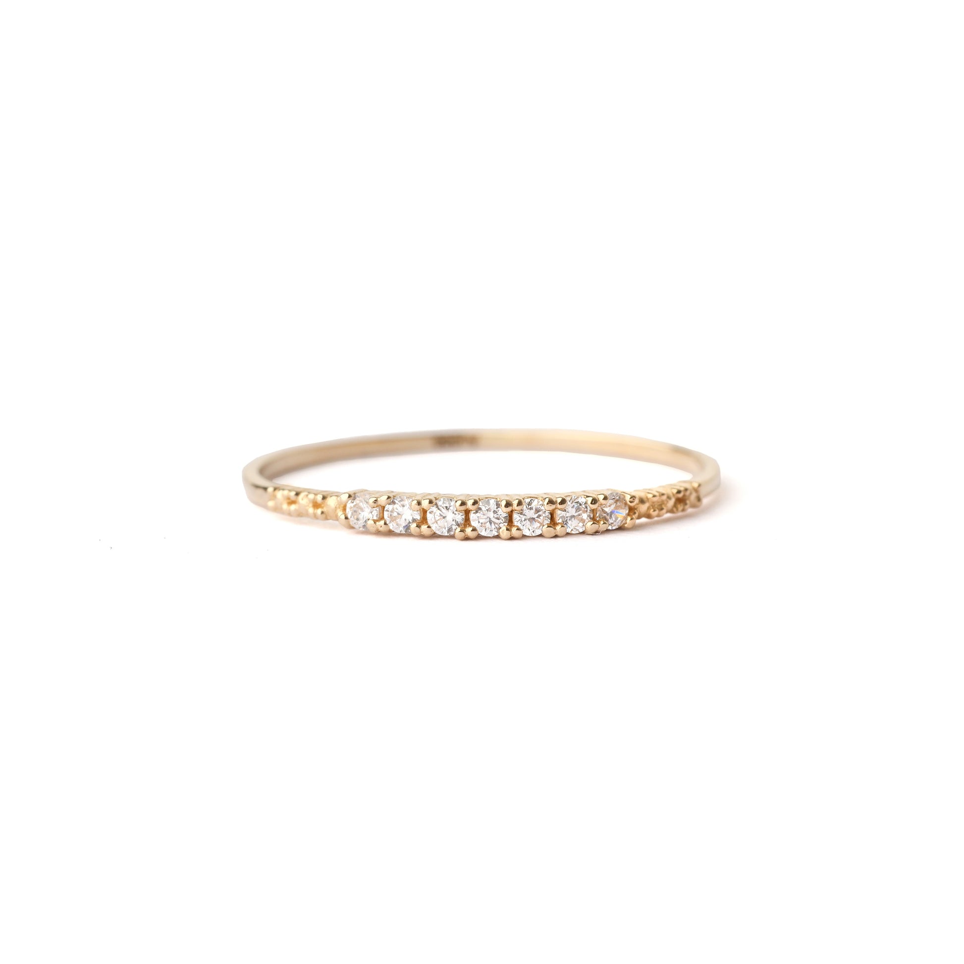 Women's solid gold ring set with a row of seven cubic zirconia gemstones on the band. The ring has detailing in the gold on the shoulders either side of the gemstones. The ring is laid flay, displayed on a white background