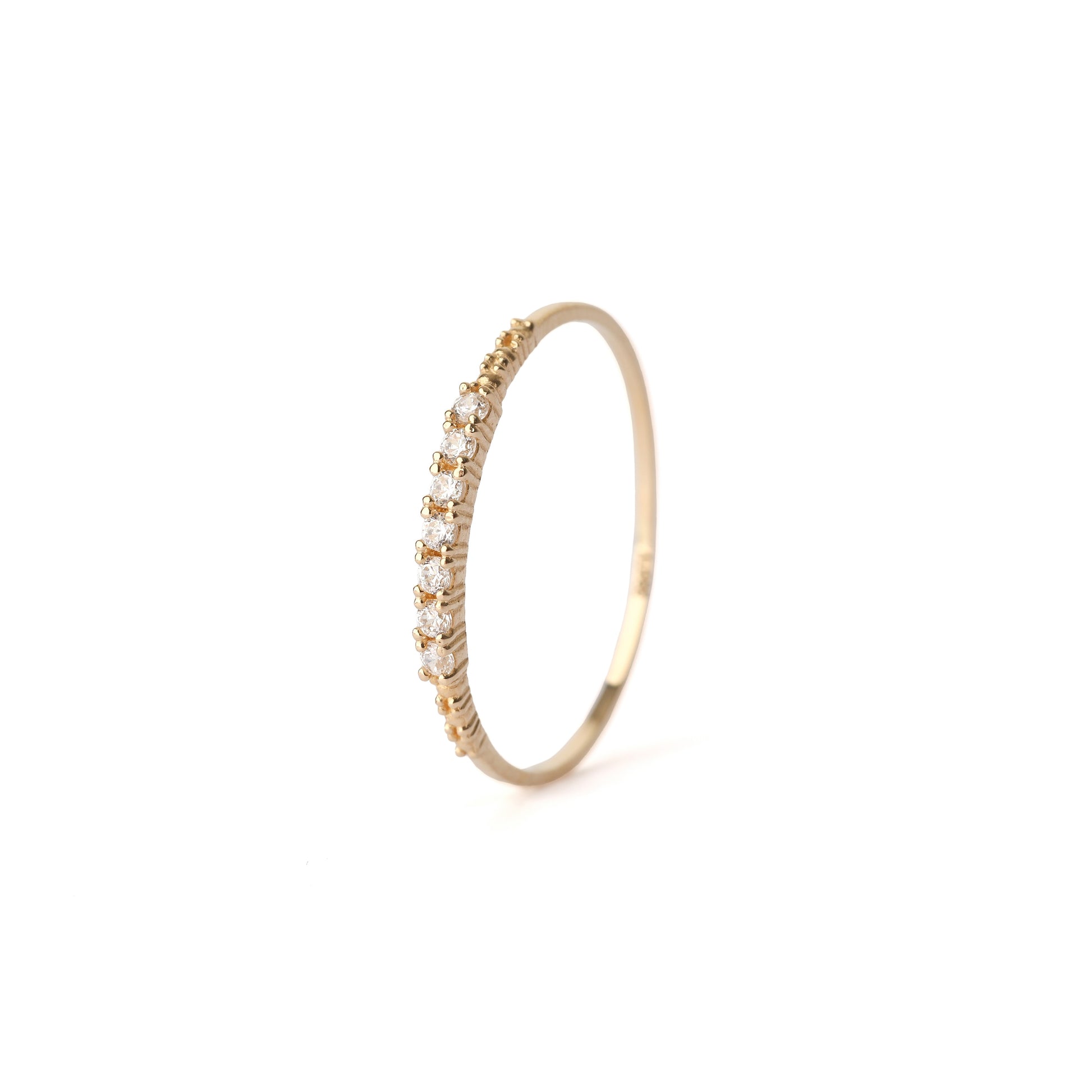 Women's solid yellow gold ring set with seven cubic zirconia gemstones around the band. The ring has detail on the in the gold on the shoulders either side of the gemstones. The ring is displayed standing upright on a white background