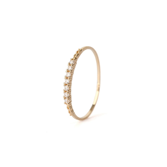 Women's solid yellow gold ring set with seven cubic zirconia gemstones around the band. The ring has detail on the in the gold on the shoulders either side of the gemstones. The ring is displayed standing upright on a white background