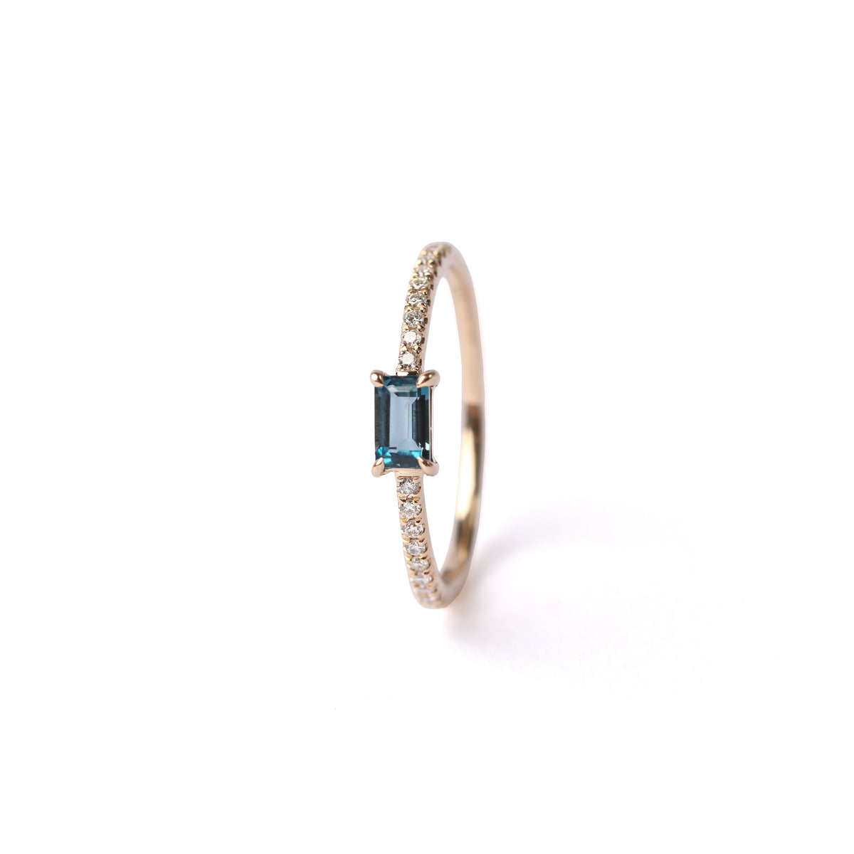 Women's solid yellow gold ring set with a central London blue topaz gemstone and small round diamonds on the shoulders each side of the topaz, displayed on a white background facing front and upright on it's side.
