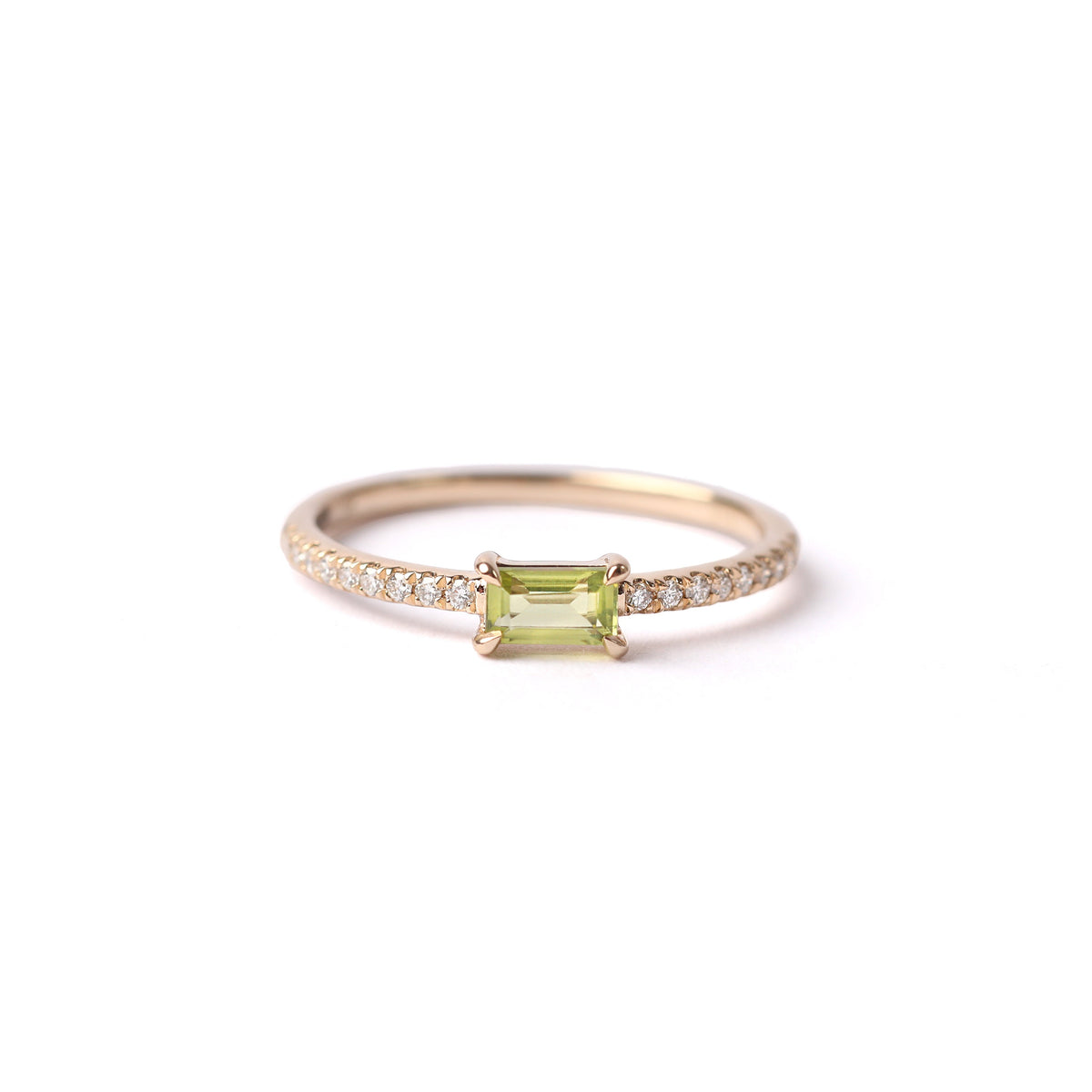 Women's solid yellow gold ring set with a central green peridot gemstone and small round diamonds on the shoulders each side of the peridot, displayed on a white background laying on it's side facing frontwards.