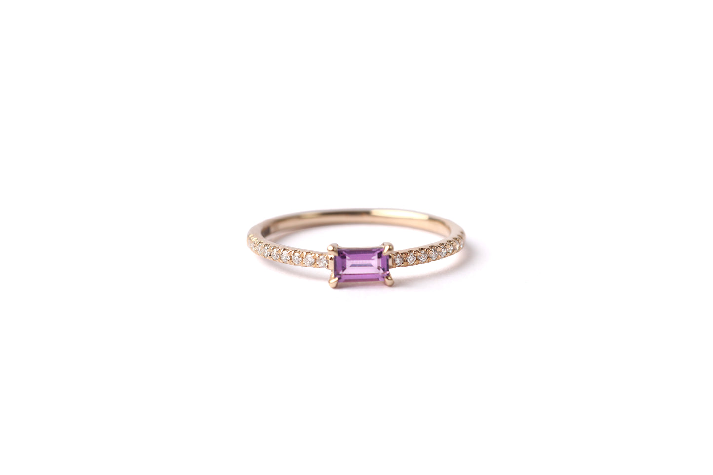 Women's solid yellow gold ring set with a central purple amethyst gemstone and small round diamonds on the shoulders each side of the amethyst, displayed on a white background laying on it's side facing frontwards.